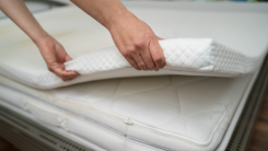 A person removing a lightly stained mattress topper from their mattress.