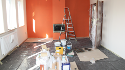 a room in the middle of renovation with paint cans on the floor and a ladder nearby