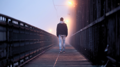 A photograph of a man from behind walking on a misty boardwalk