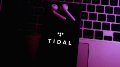 A phone showing the Tidal logo, lying on a laptop keyboard