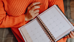 A photograph of a woman wearing an orange sweater, planning to write in her weekly calendar