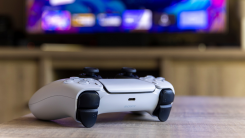 A photograph of a PS5 controller on a coffee table. Behind it, out of focus, is a television.