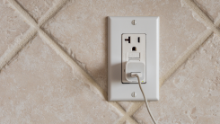 three-pronged outlet on a tile wall with a charger plugged in