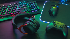 A photograph of a keyboard, mouse, headphones, and gamepad on a desk bathed in colorful light.