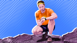 A man kneeling on a rocky surface and checking his fitness tracker