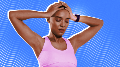 A woman in workout clothes and wearing a fitness tracker looking exasperated with her hands on her head