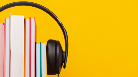 A small pile of books standing horizontally aith a pair of over-ear headphones stretched around them