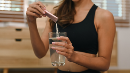 A woman adding collagen powder to a glass of water