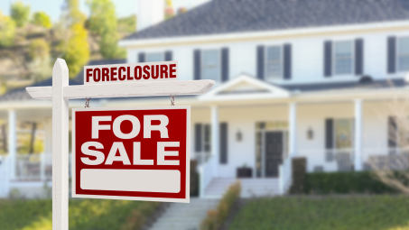 A photograph of a "foreclosure for sale" sign in front of a large, Colonial-style white house