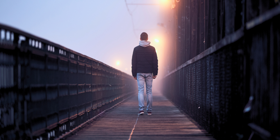 A photograph of a man from behind walking on a misty boardwalk