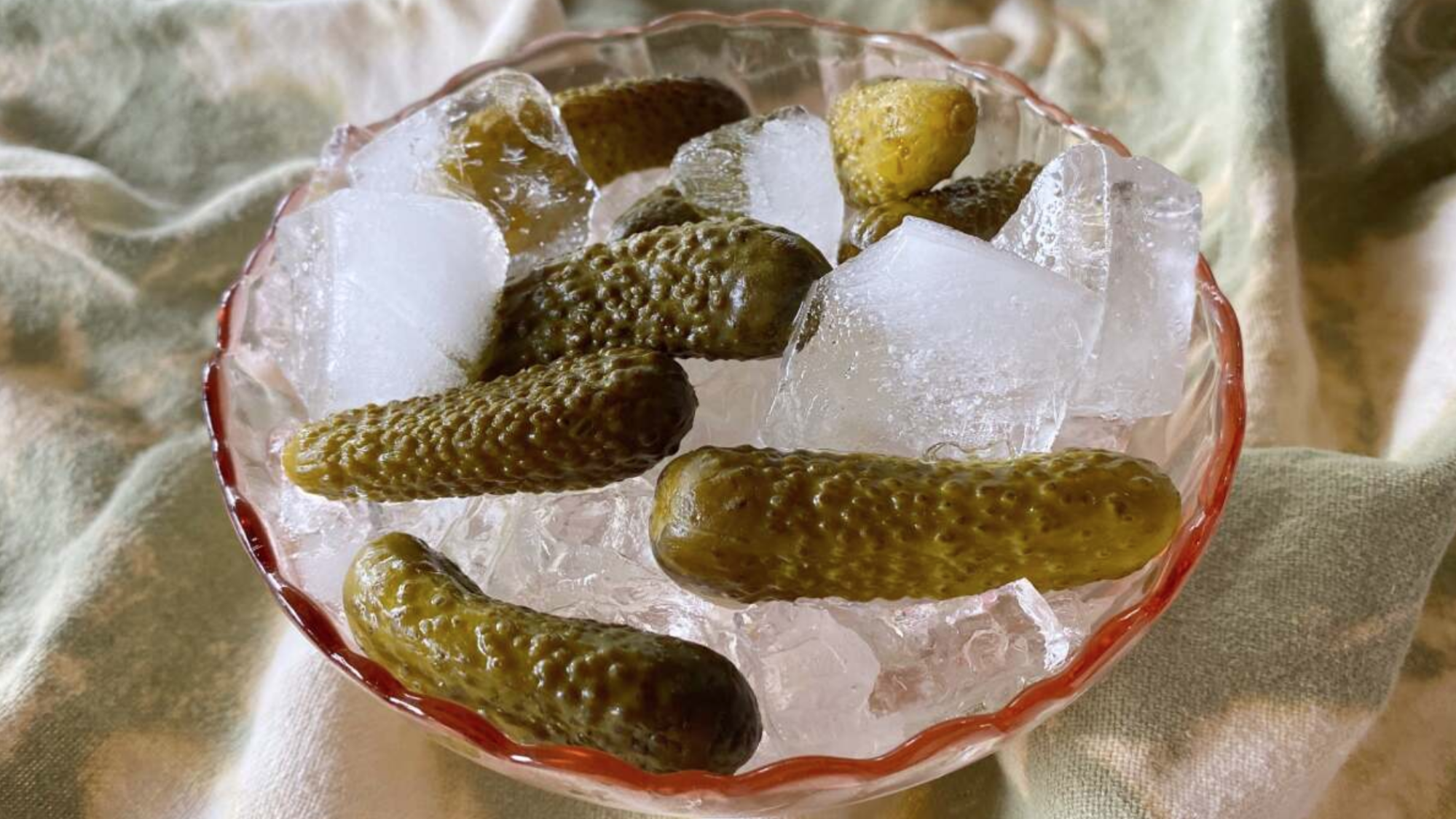 A bowl of ice with pickles on top.